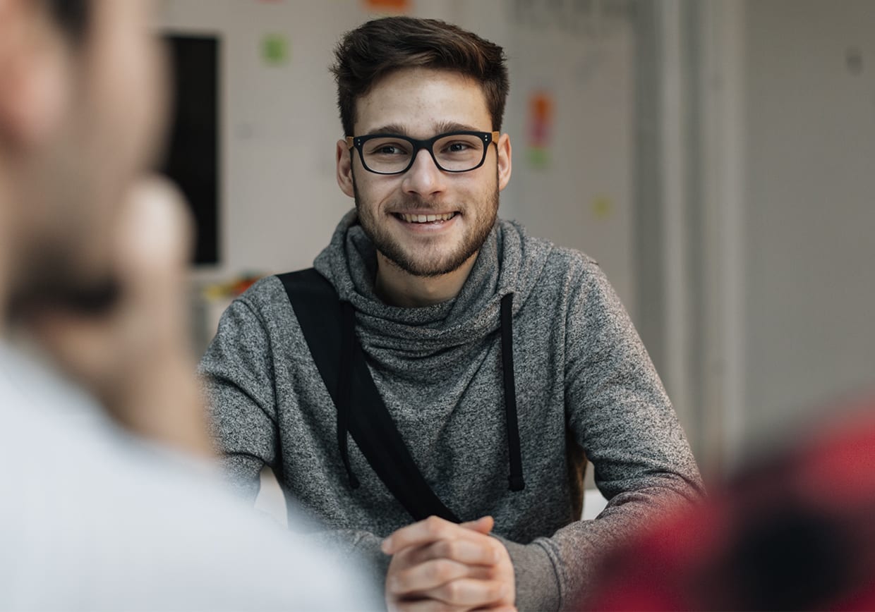 Young man at a job interview talking with two developers. They are running startup developer company from their home. Selective focus to young candidate over their shoulders.